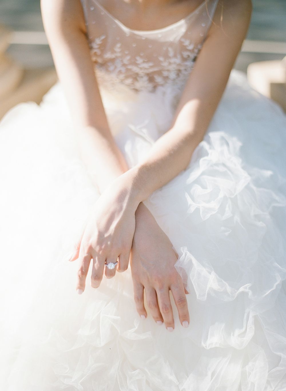 Delicate detail shot of hands resting on white tulle wedding gown.