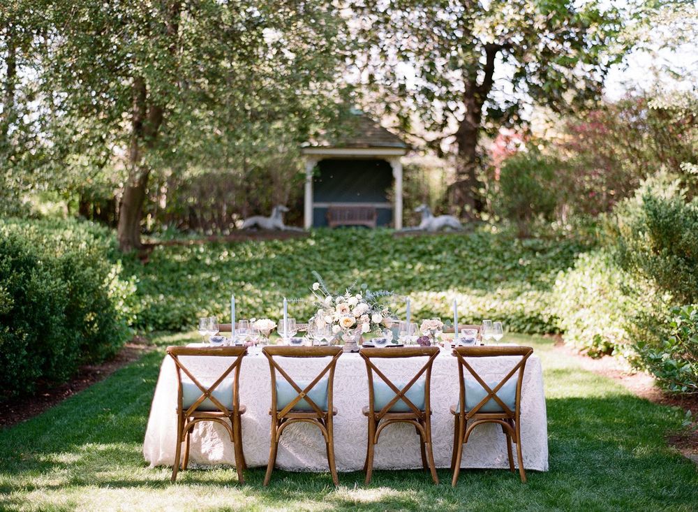 Elegant outdoor wedding table setup with rustic wooden chairs in a garden setting.