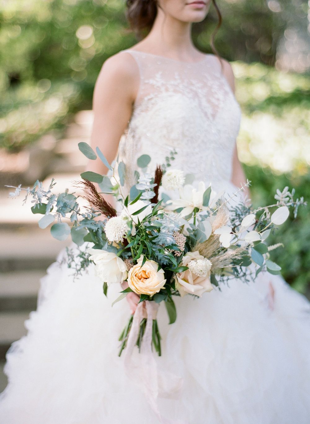Wedding bouquet featuring peach roses and eucalyptus leaves held against a white lace dress.