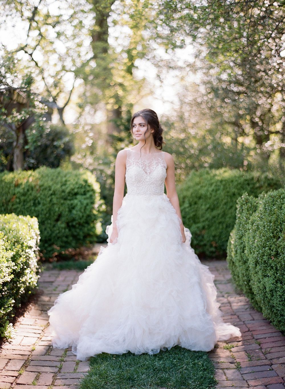 Garden bridal portrait on a brick pathway with manicured hedges and trees in the background.