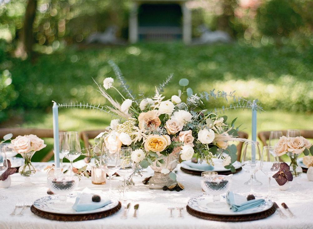 Elegant garden wedding table setting with peach and white floral centerpiece and blue accents.