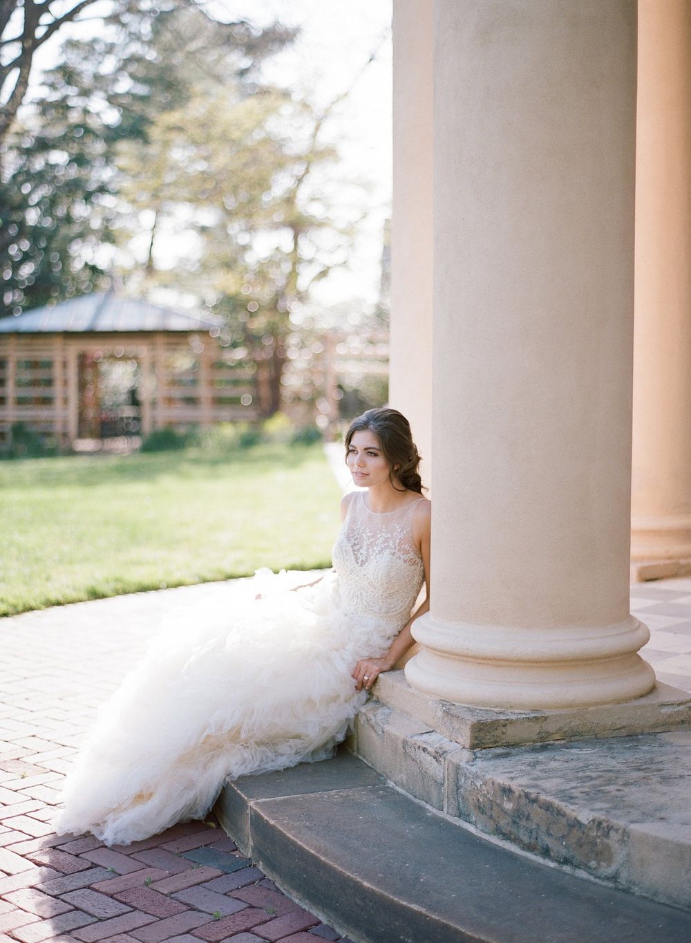 Classic white wedding gown with lace details shown near an elegant column on stone steps.