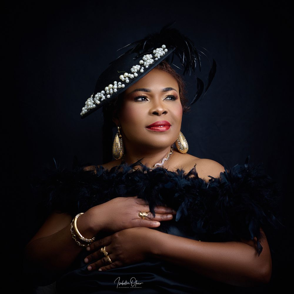 Studio portrait in dramatic lighting featuring elegant Nigerian formal wear and statement hat.