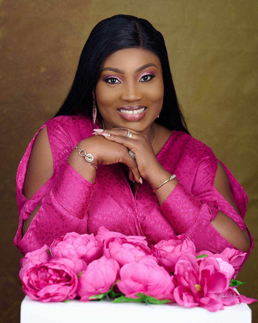Elegant portrait against pink roses featuring a woman in a fuchsia dress with jewelry.