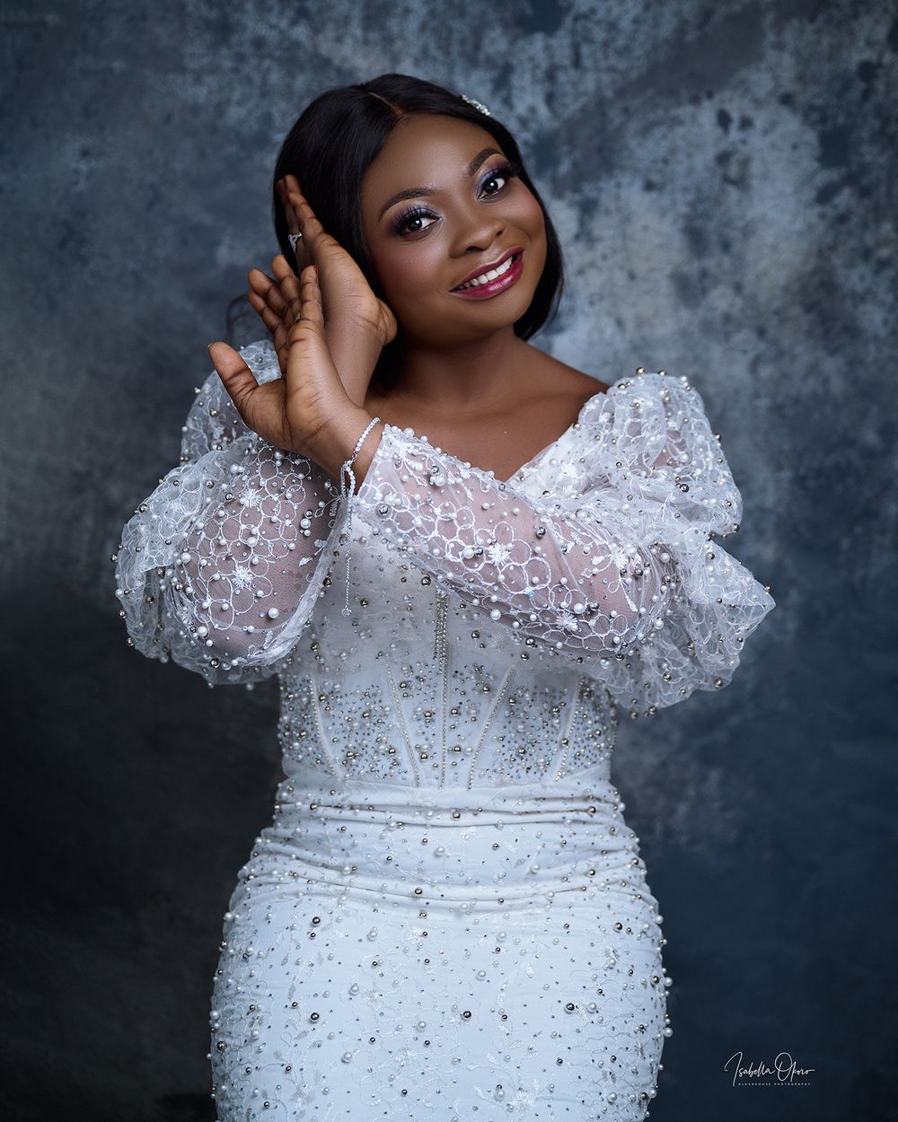 Glamorous portrait featuring a sparkly white dress with puffy sleeves against textured grey background.