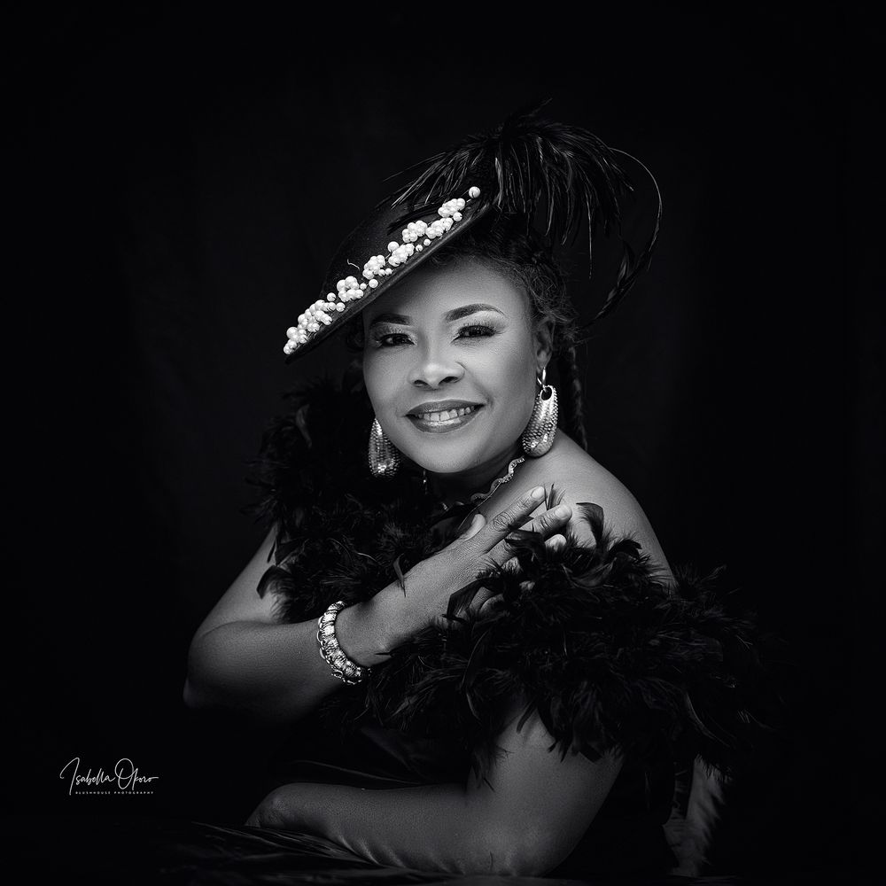 Professional studio portrait against black background featuring elegant feather accessories and jewelry.