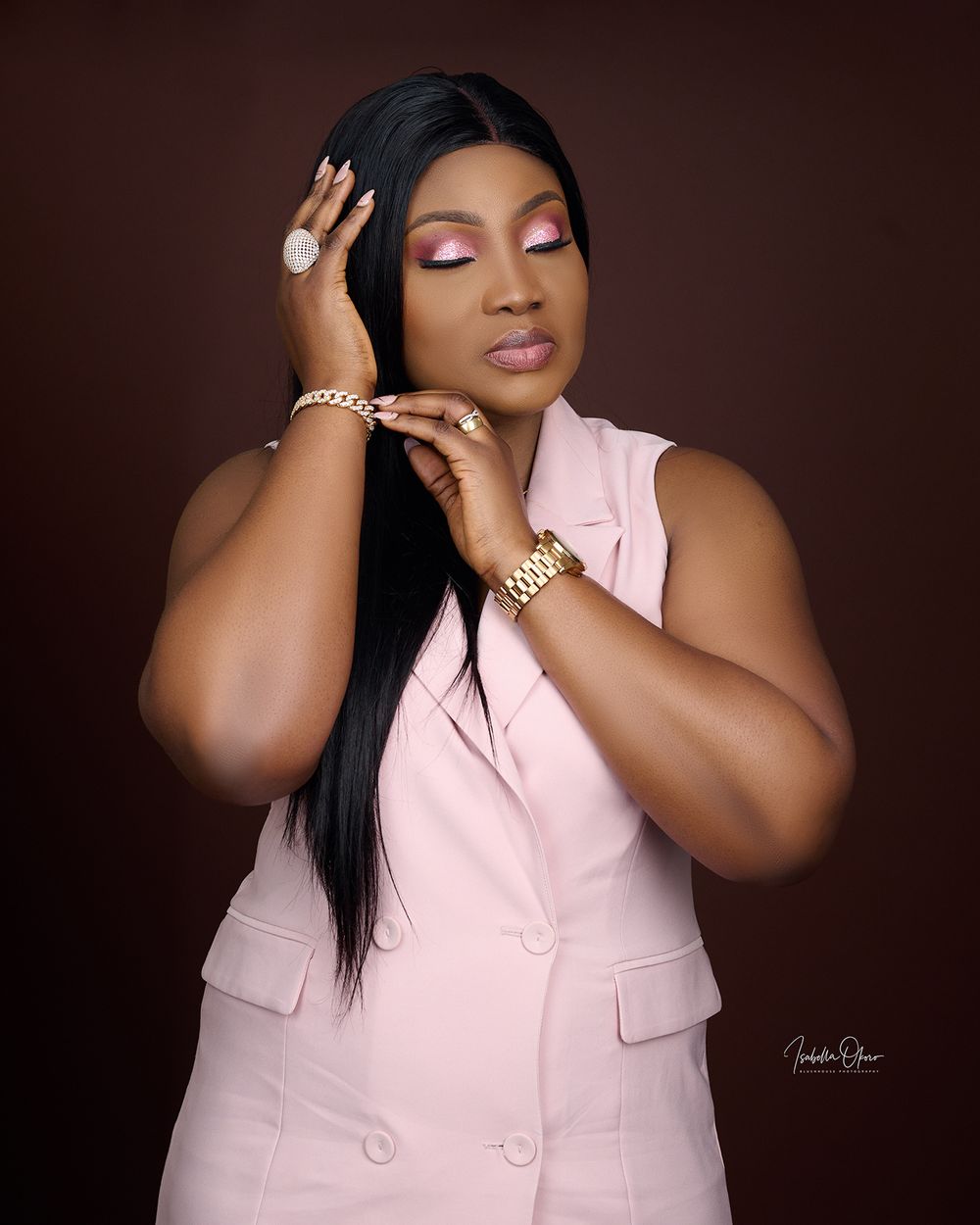 Studio portrait of a woman in a pink blazer wearing jewelry and posing with closed eyes.
