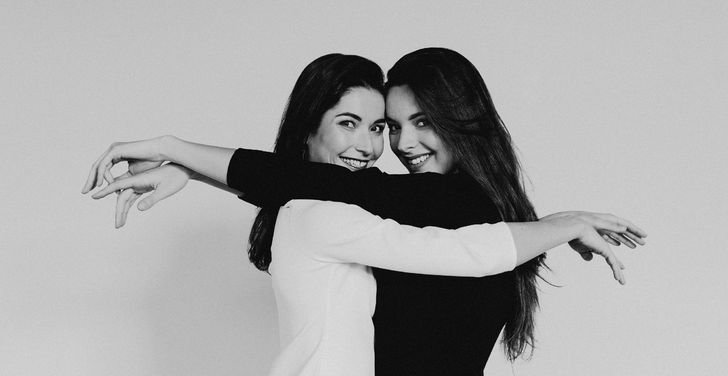 Black and white portrait of two friends posing playfully with outstretched arms.