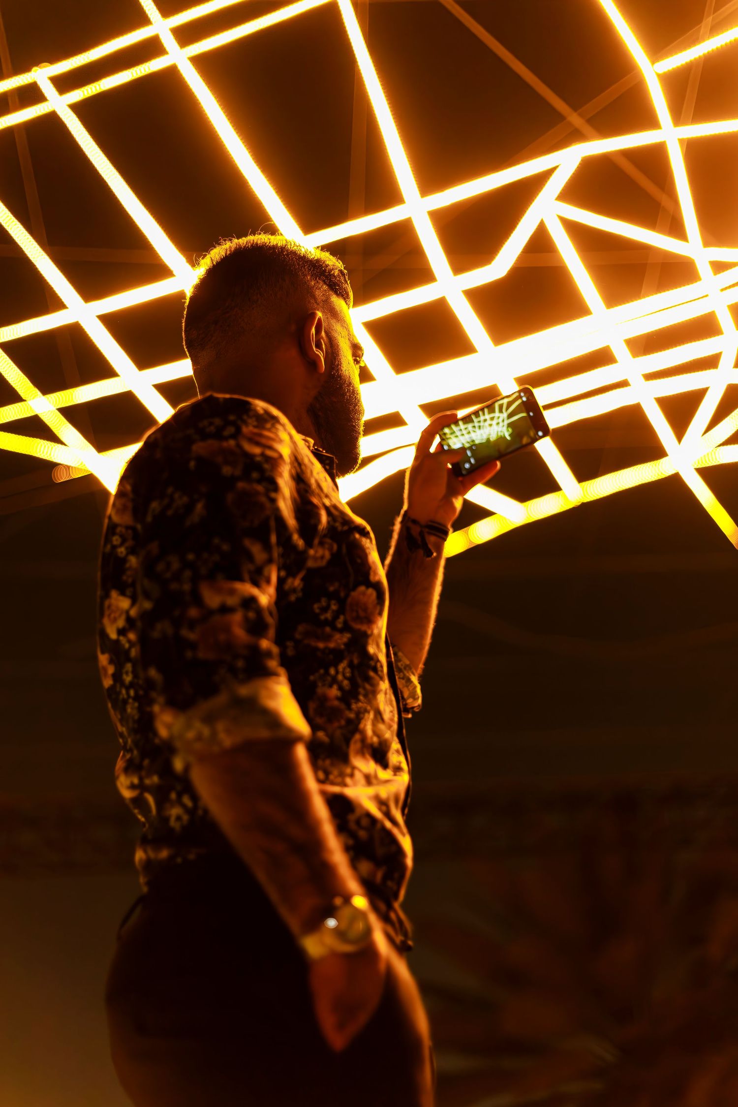 Person in a patterned shirt stands beneath illuminated geometric ceiling lights creating striking patterns.