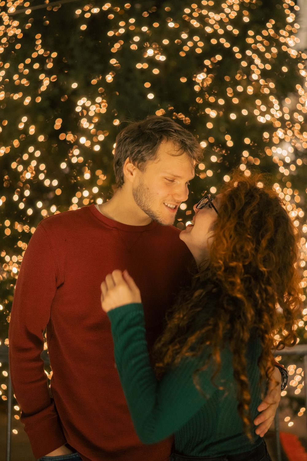 A romantic couple shares intimate moments against a backdrop of twinkling holiday lights.