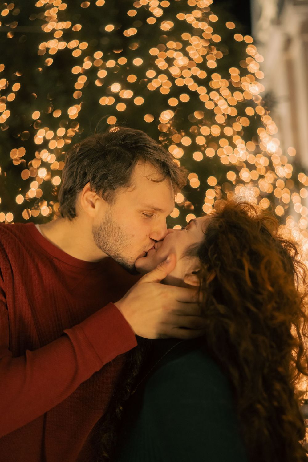 A couple embraces in front of sparkling golden bokeh lights during an evening photoshoot.