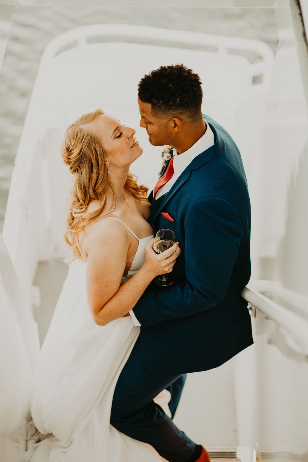 Bride and groom gaze lovingly at each other while embracing on a white boat during their wedding.