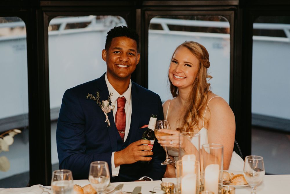 Happy couple toasting with champagne bottle at wedding reception aboard a boat venue.