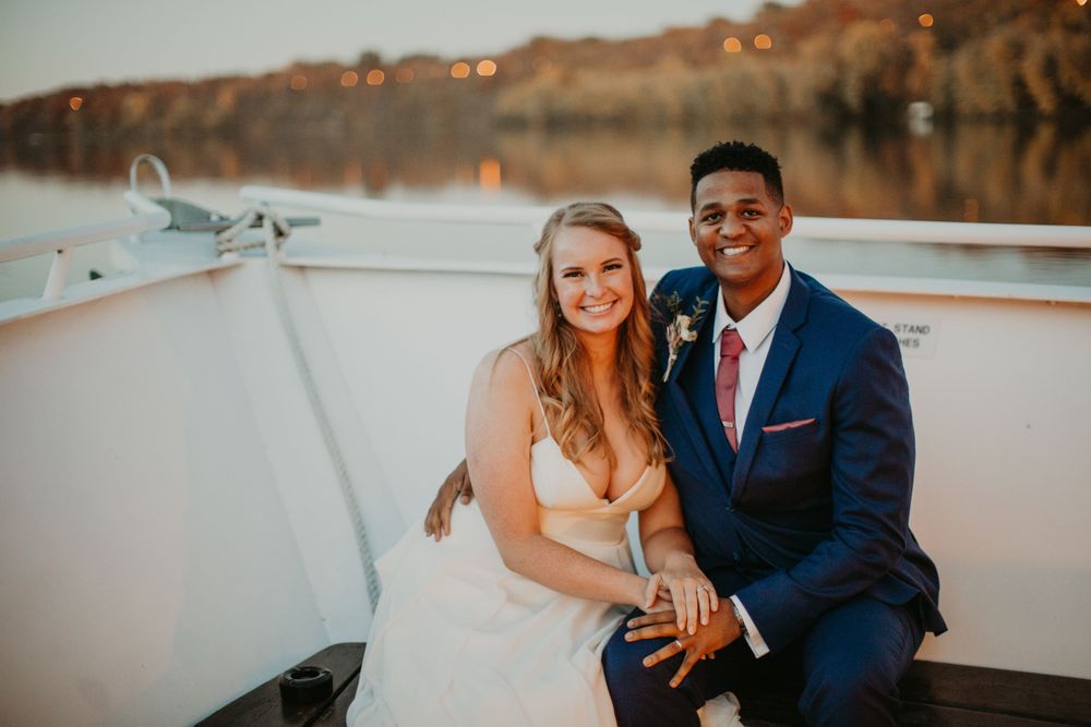 Bride and groom sitting on boat deck at sunset with lake view, groom in navy suit.