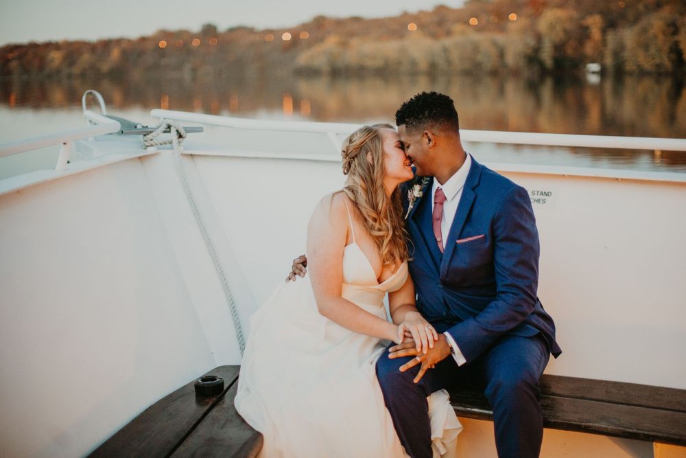 Bride and groom sharing a romantic kiss on boat deck at sunset over calm lake waters.