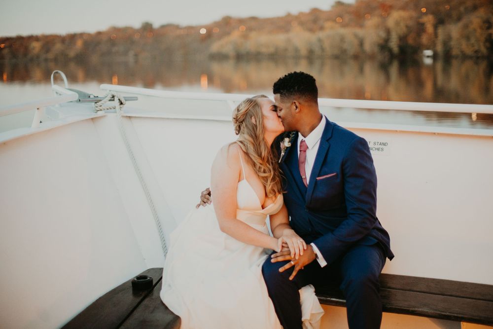 Newlyweds kissing on boat deck during golden hour with beautiful autumn lake backdrop.