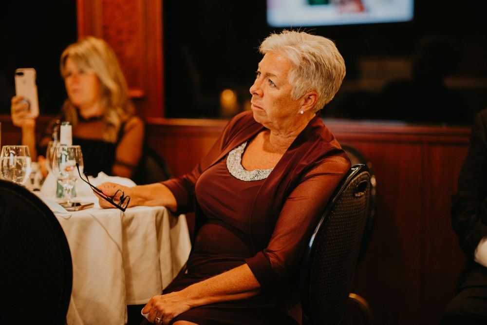 Elegant older woman with short white hair in burgundy top seated at wedding reception dinner table.