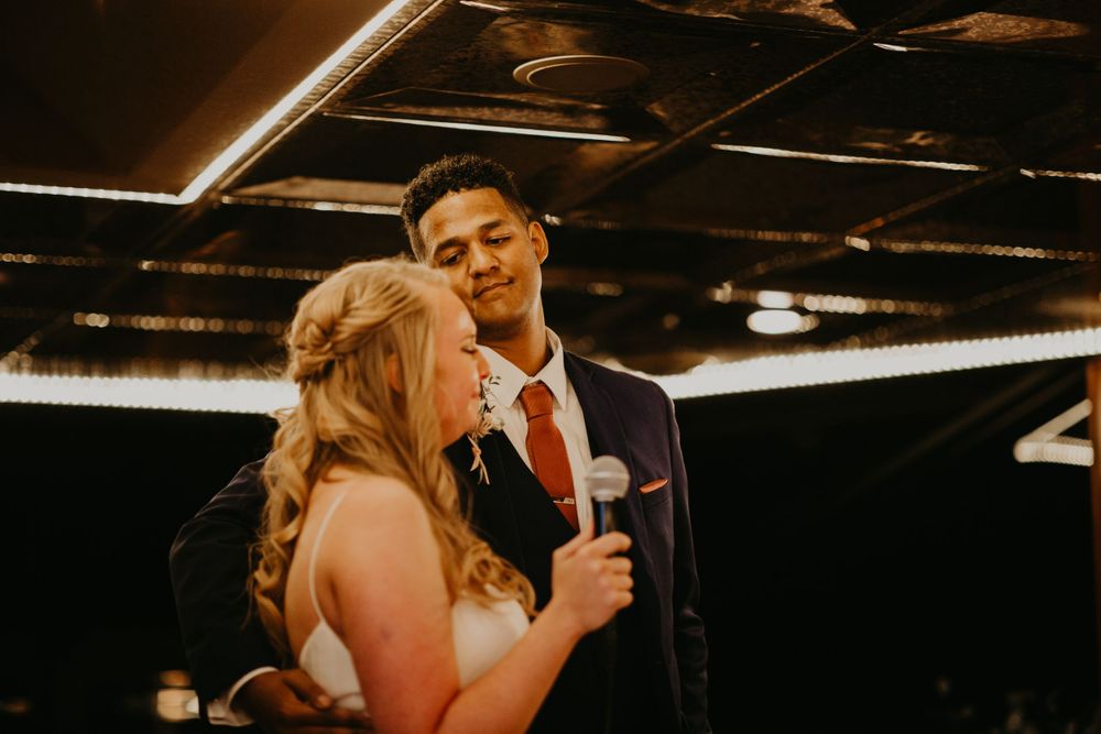 Bride and groom sharing microphone during wedding reception speech at elegant venue.