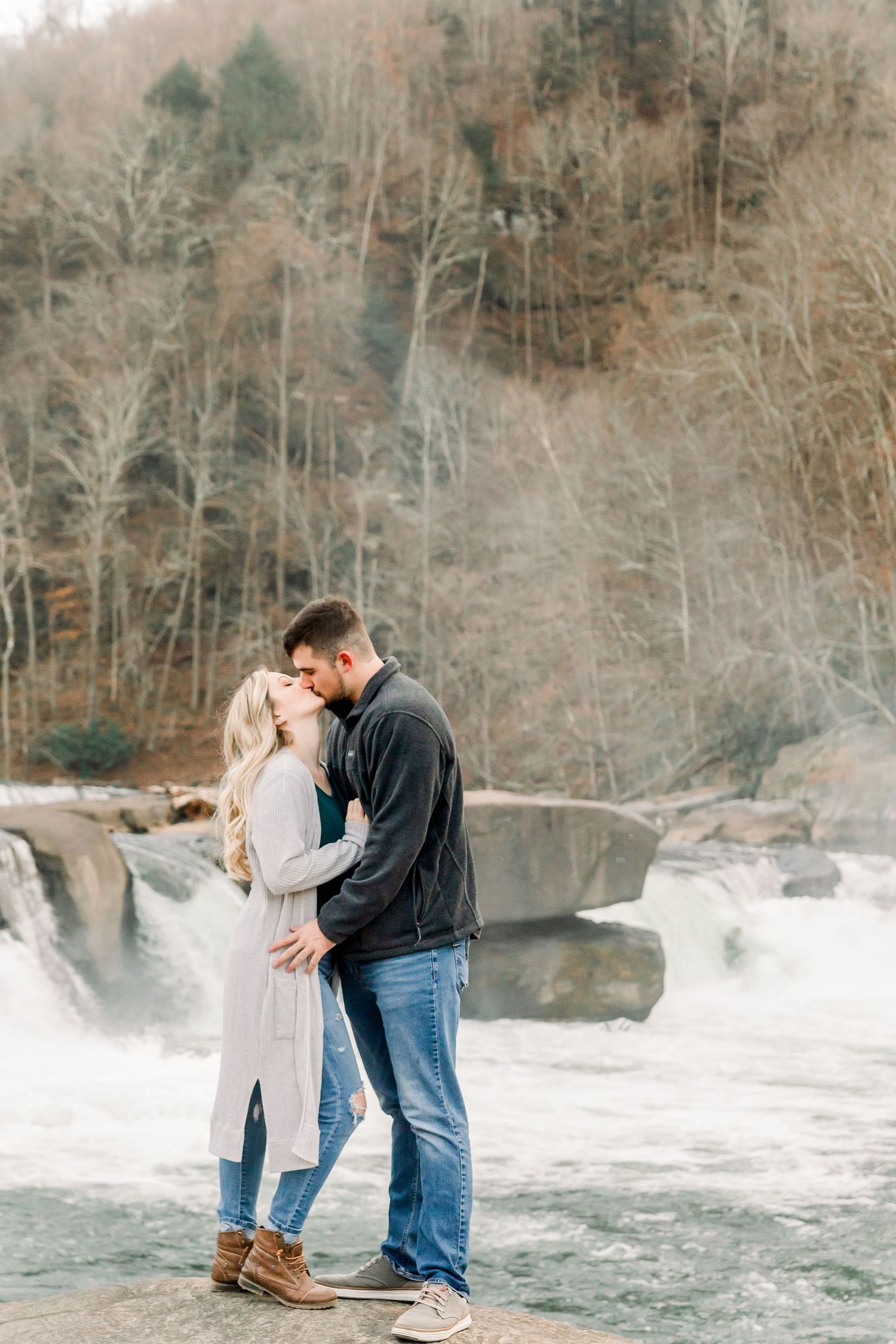 Couple shares romantic moment by rushing waterfall in winter engagement photos.