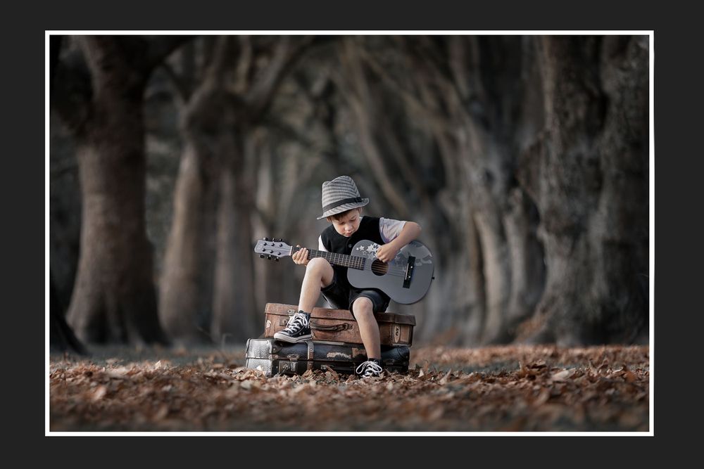 Person playing guitar while sitting on ground in moody forest setting.