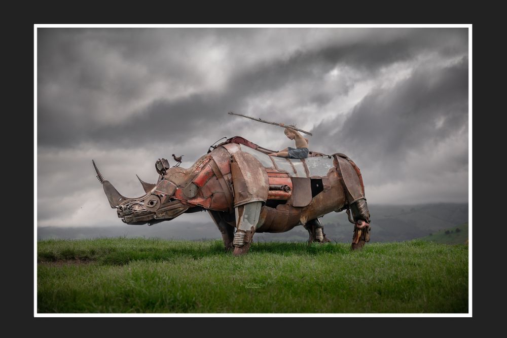 Steampunk-style mechanical rhino sculpture against stormy sky in grassy field.