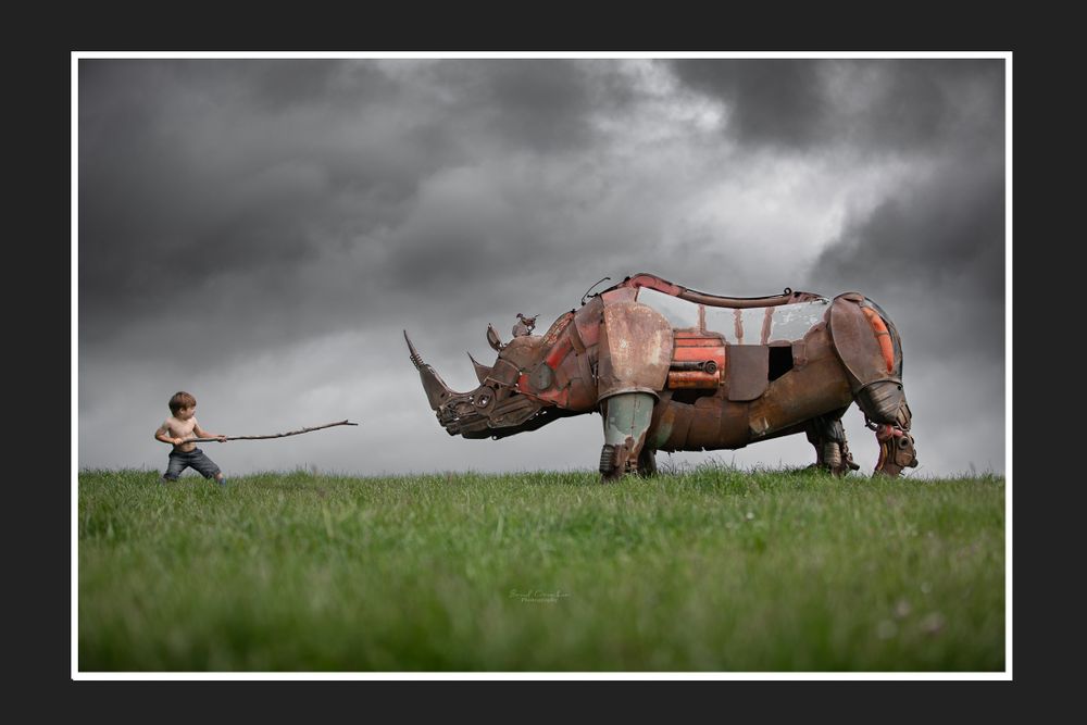 Creative photography of a mechanical rhino being pulled by small figure in a field.