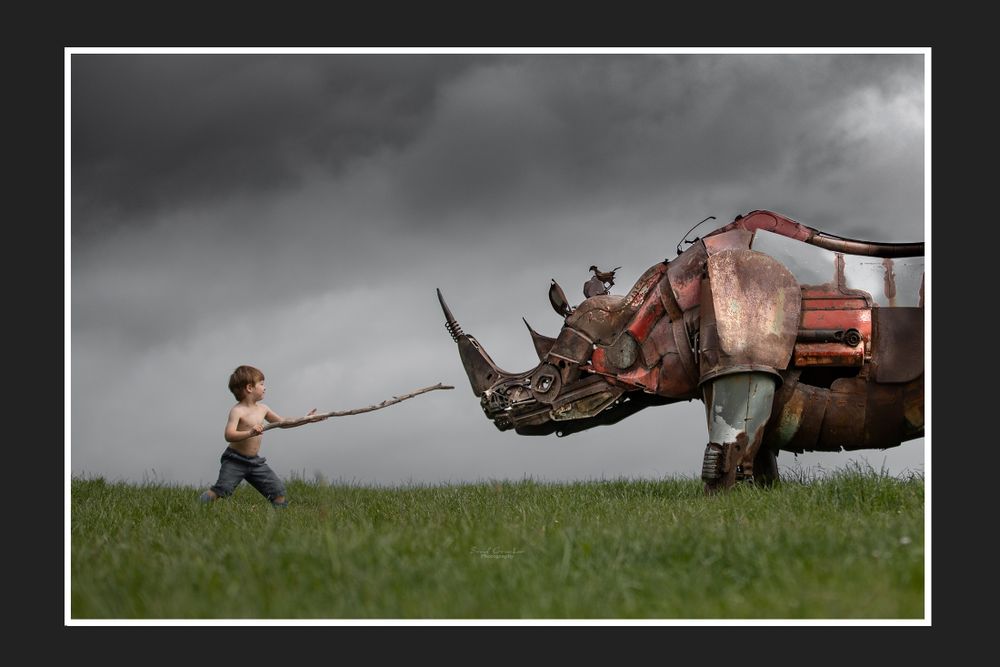 Artistic photo of small figure pulling large mechanical rhino in dramatic landscape.