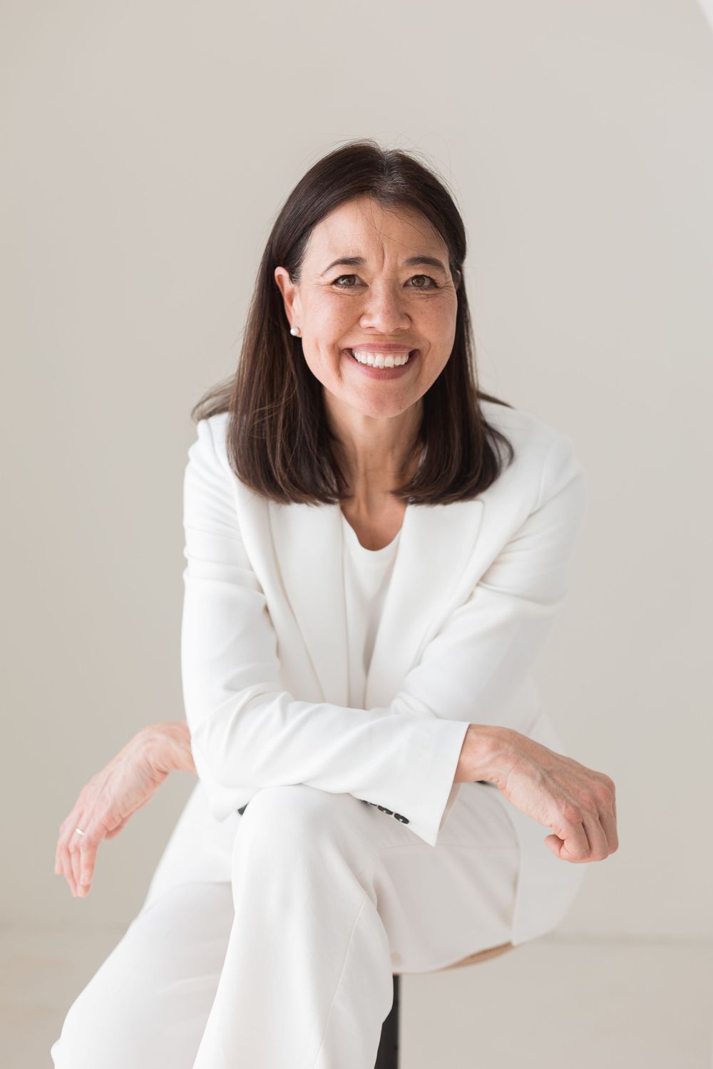 Smiling older woman in white suit seated against neutral background.
