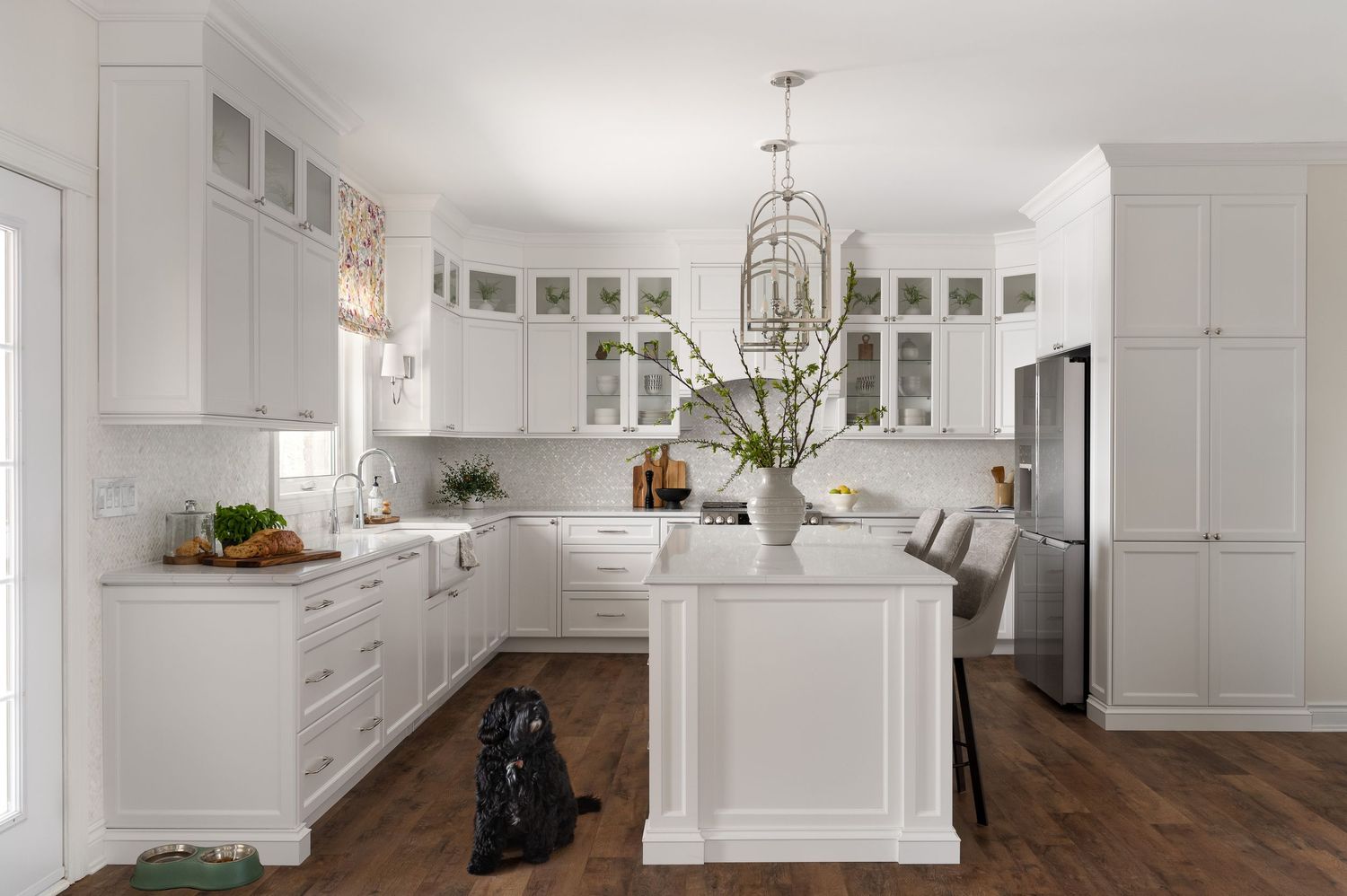 Bright white modern kitchen with glass cabinets, chandelier and hardwood floors.