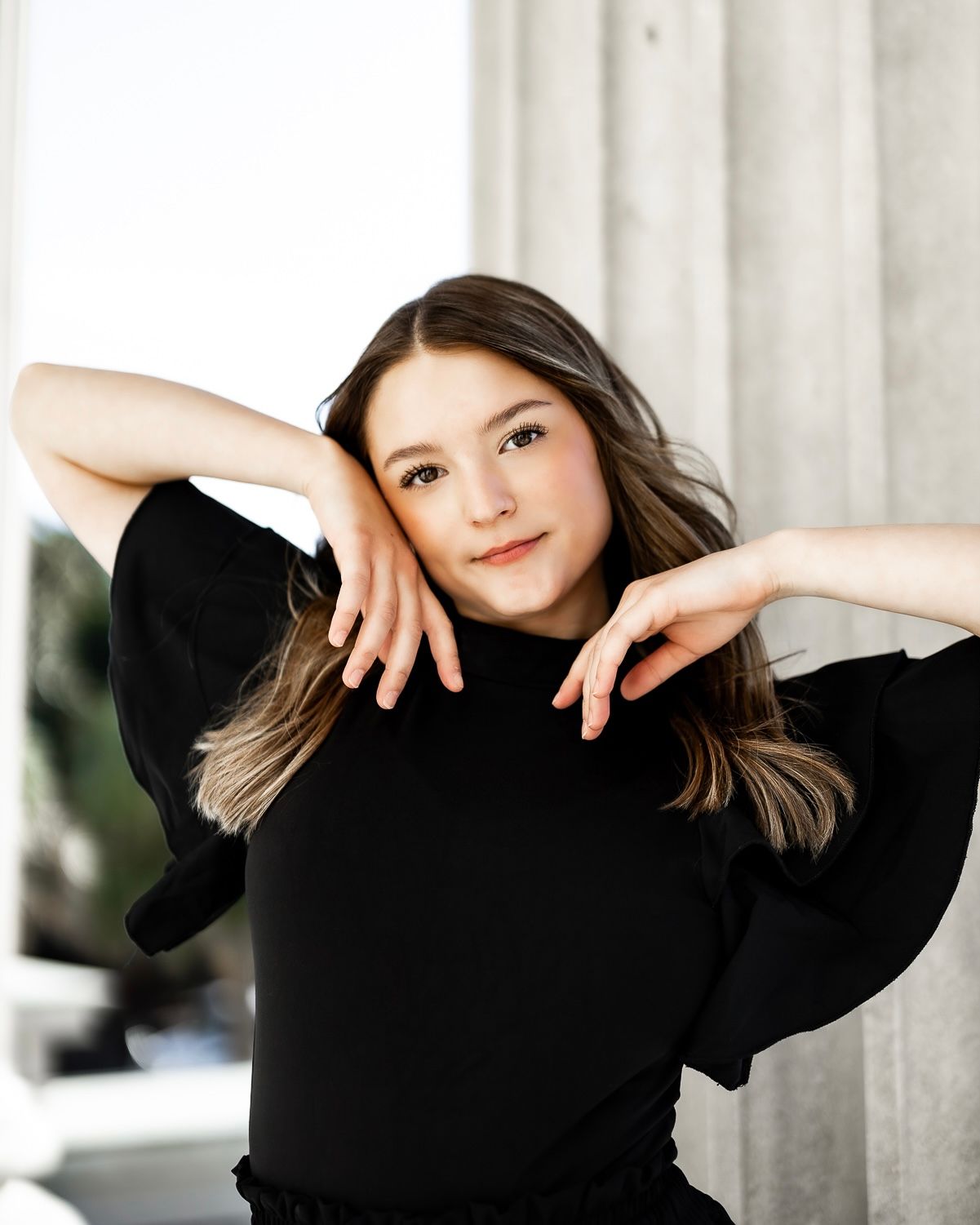 Artistic portrait of a person in a black sweater posing gracefully against a light background.