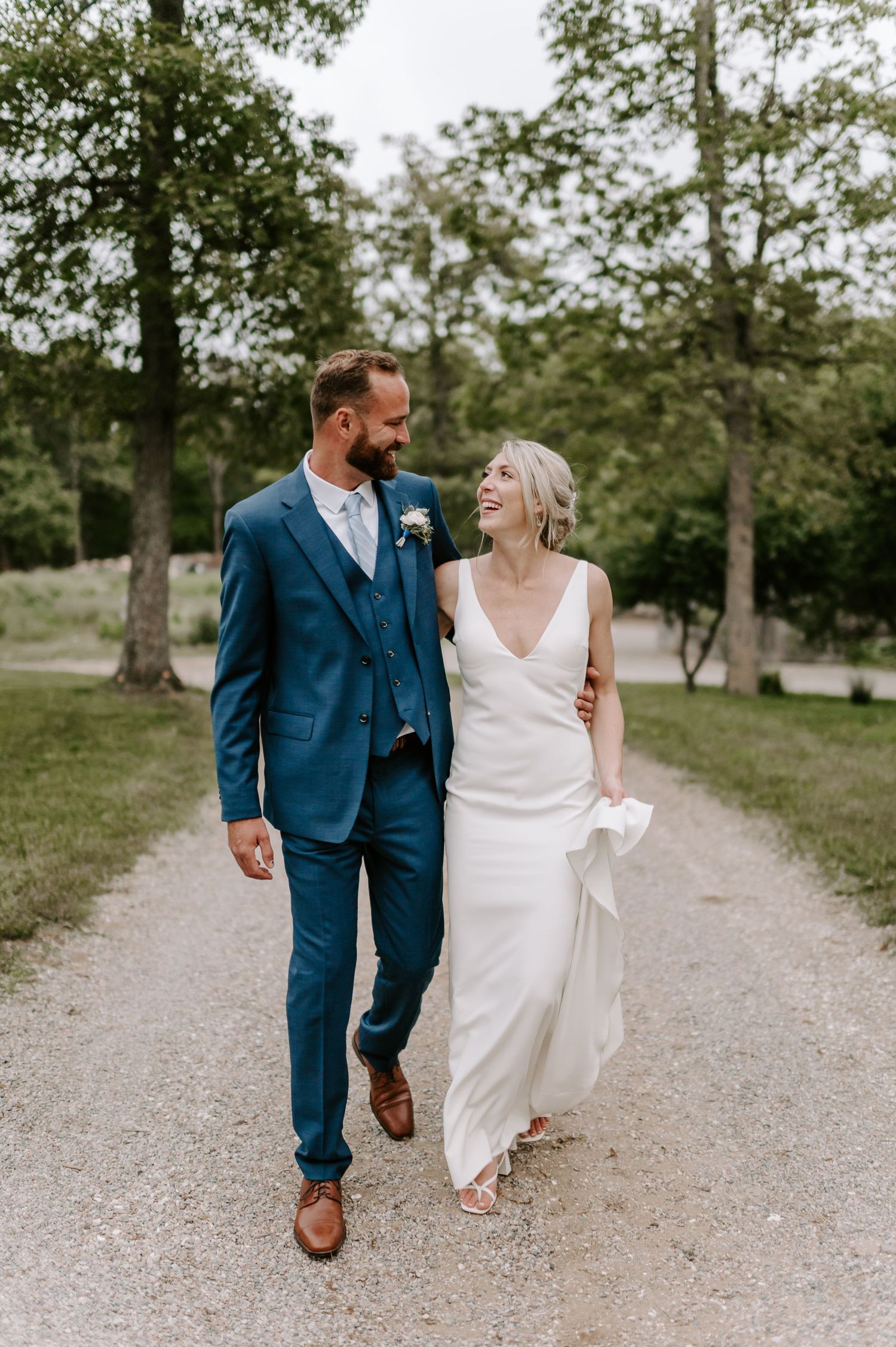 A couple strolls together on a winding gravel path surrounded by greenery.