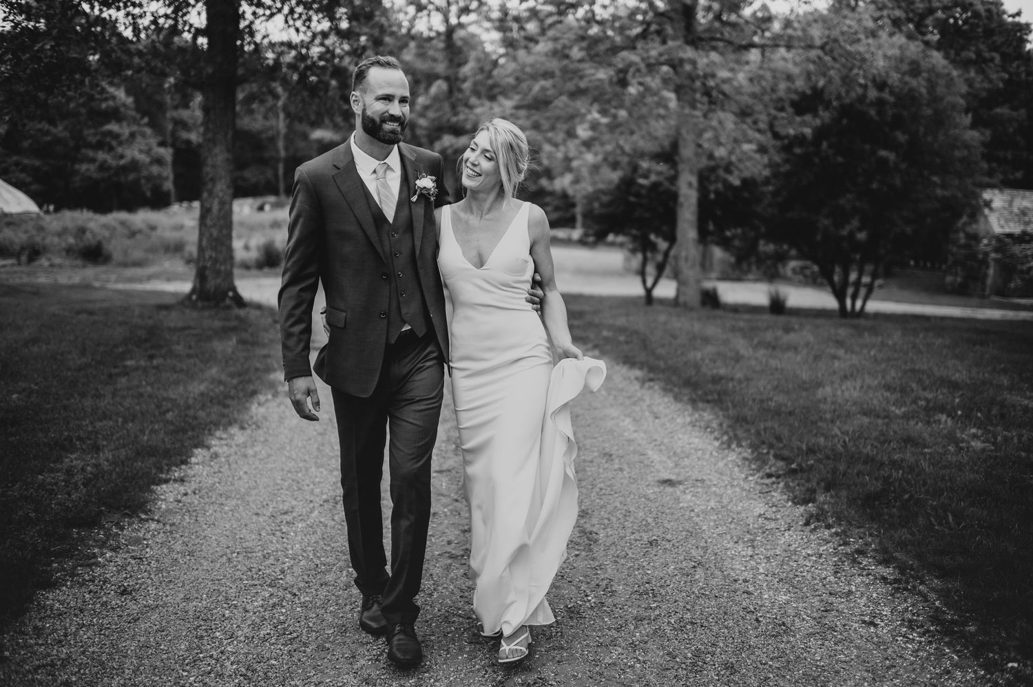A couple walks hand in hand down a scenic gravel path in black and white.