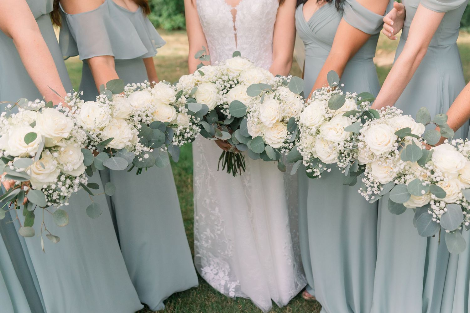 Row of bridesmaids holding elegant white and green bouquets against light blue dresses.