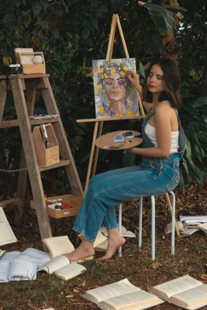 Artist workspace in garden with books, easel, and floral portrait painting.