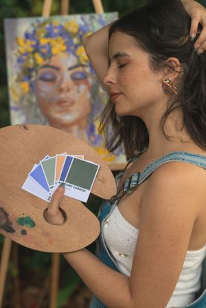 Artist holding a wooden palette with color swatches while painting outdoors.