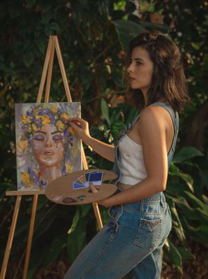 Artist painting at an easel outdoors while holding a wooden palette.