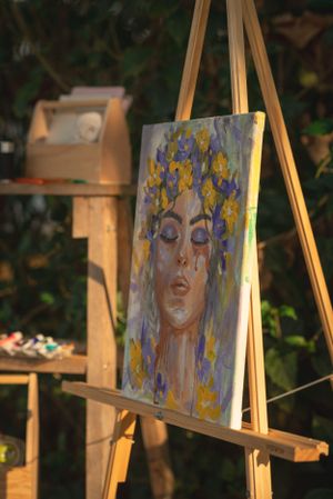 Portrait painting with yellow and purple floral crown displayed on wooden easel at dusk.