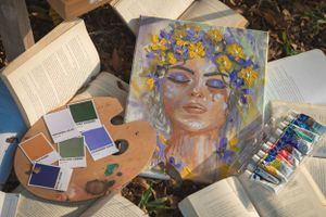 Artistic setup with paint supplies, books, and a portrait painting featuring yellow and purple flowers.
