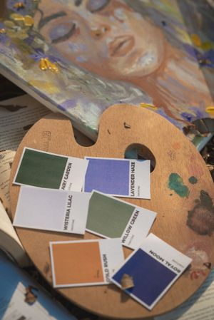 Color swatches and paint samples arranged on a wooden artist palette next to artwork.