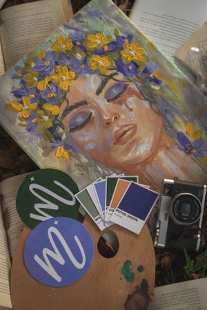 Beautiful painting of a dreamy figure wearing a floral crown displayed with color samples and vintage camera on books.