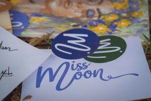 Blue and green Miss Moon branding logo on white paper with decorative elements.