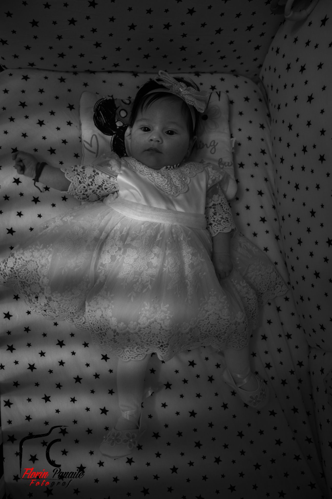 Baby in white dress lying on star-patterned fabric in black and white.