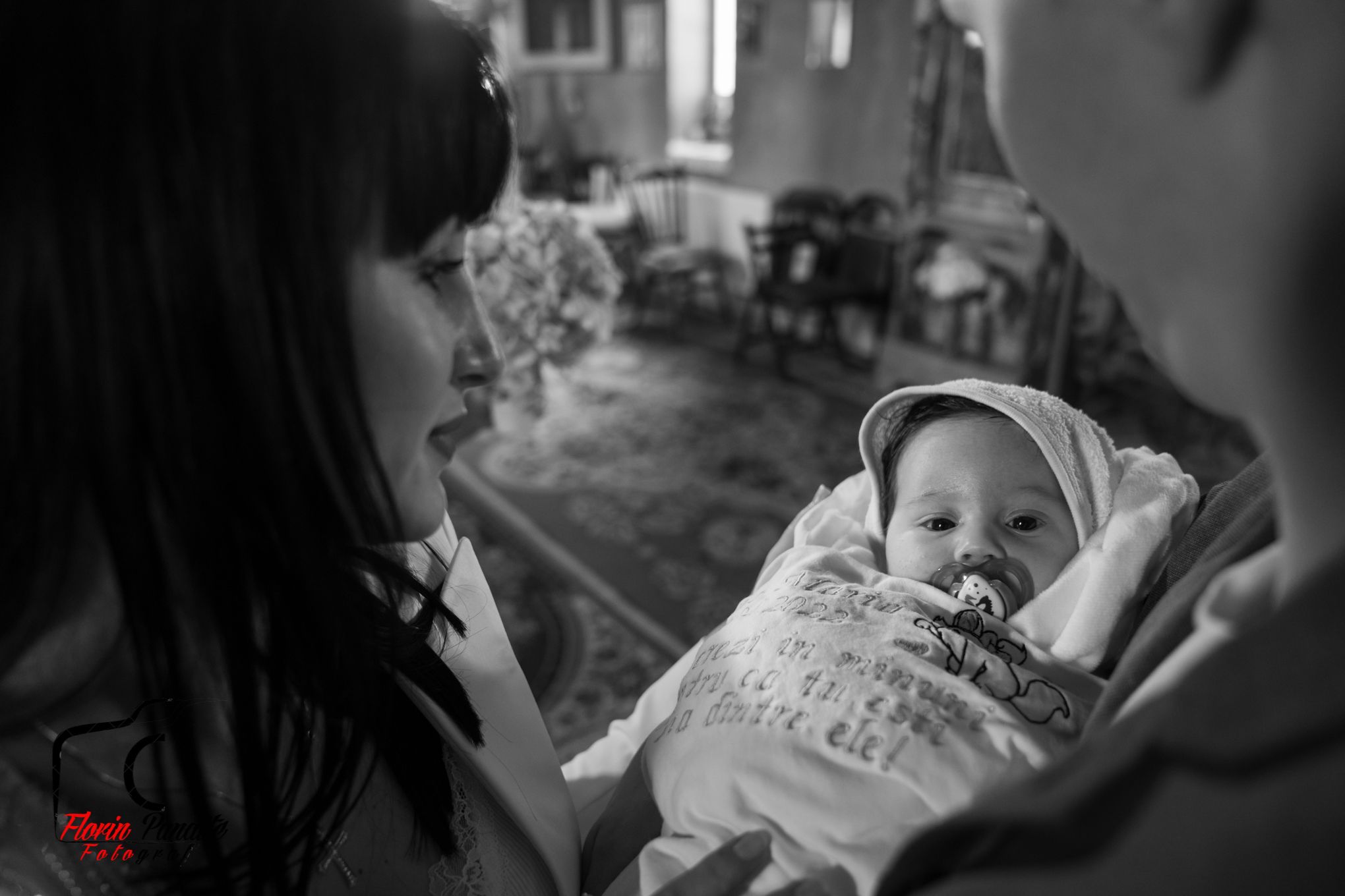 Black and white image of baby in white dress being cradled during ceremony.