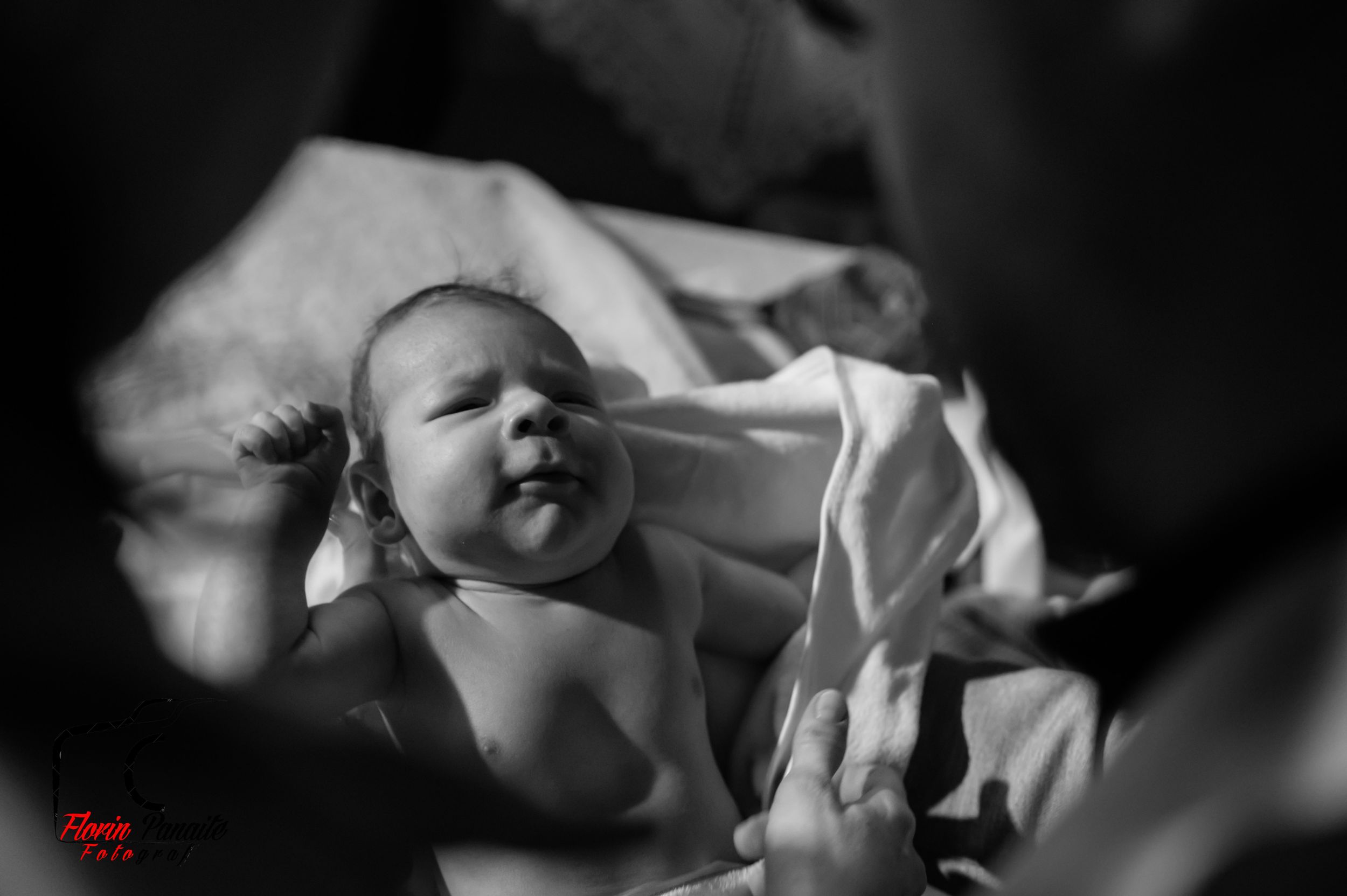 Black and white photo of newborn baby being held during baptism ceremony.