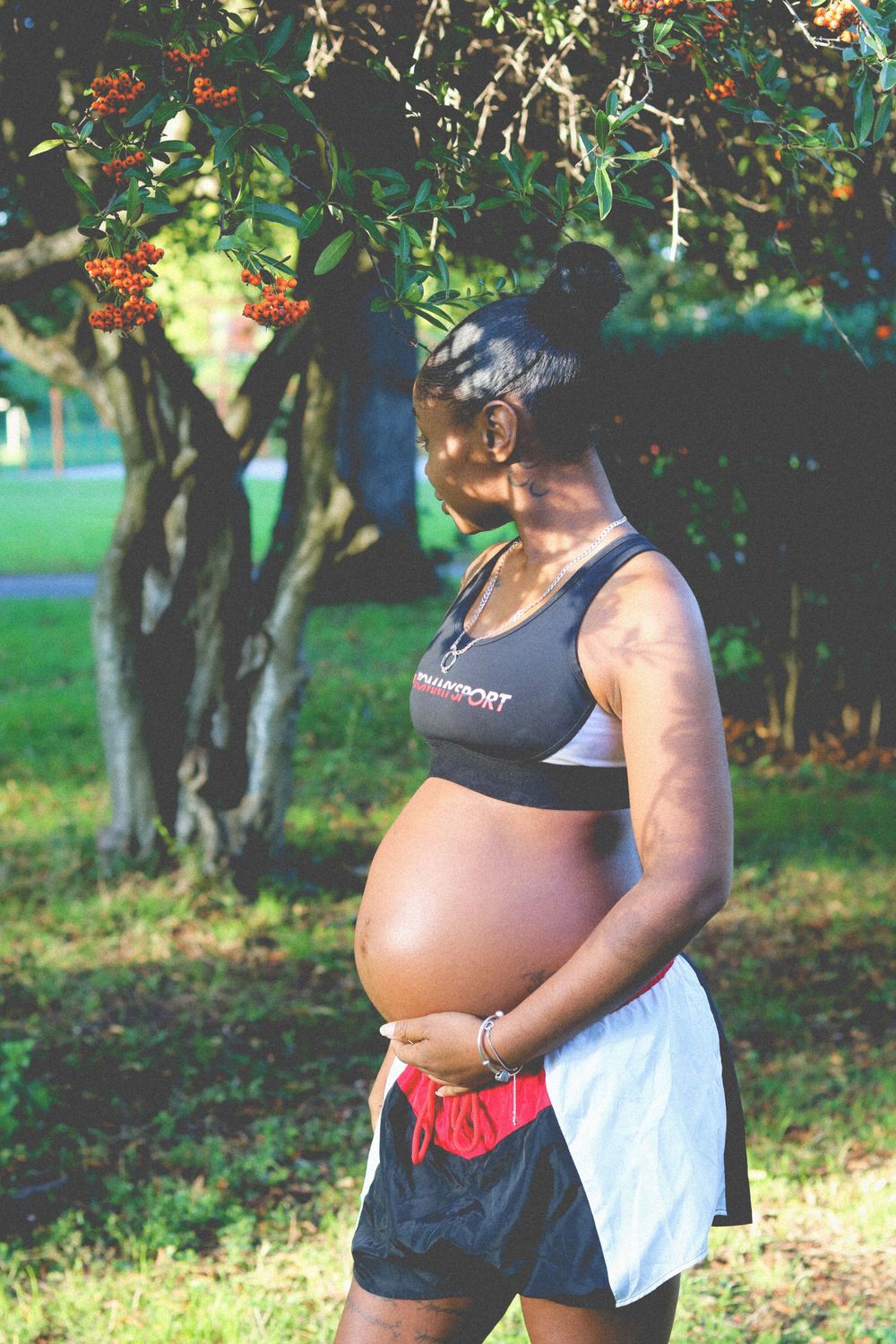 A series of photos showing the progression of a pregnancy with a person wearing athletic wear in an outdoor garden setting.