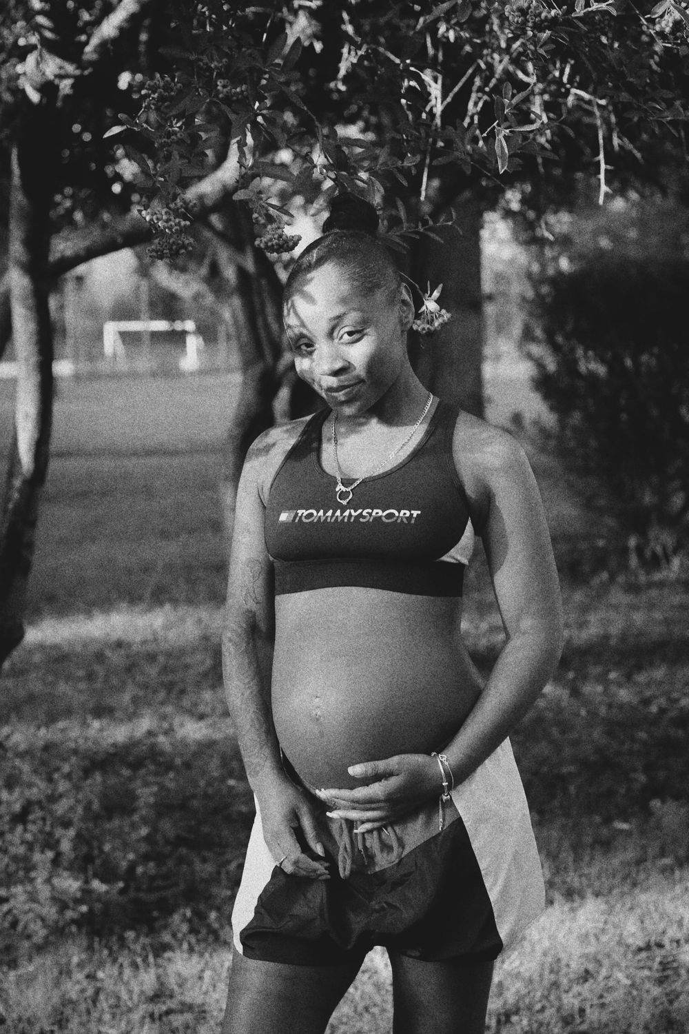 A black and white photo series showing a pregnant woman in athletic wear posing outdoors in a natural setting.