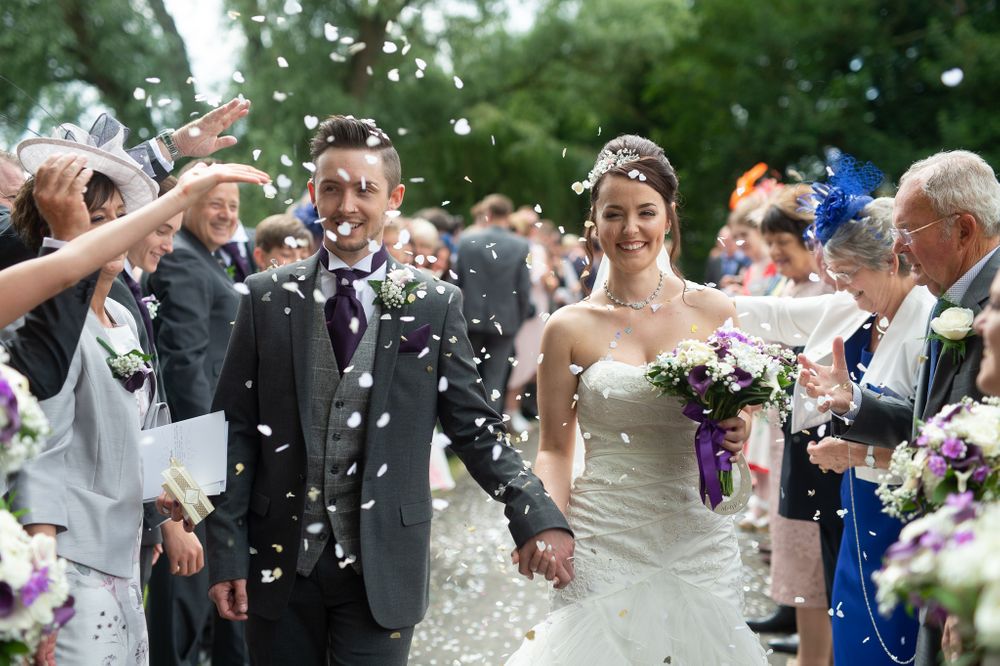 Wedding couple walking through shower of confetti surrounded by celebrating guests.