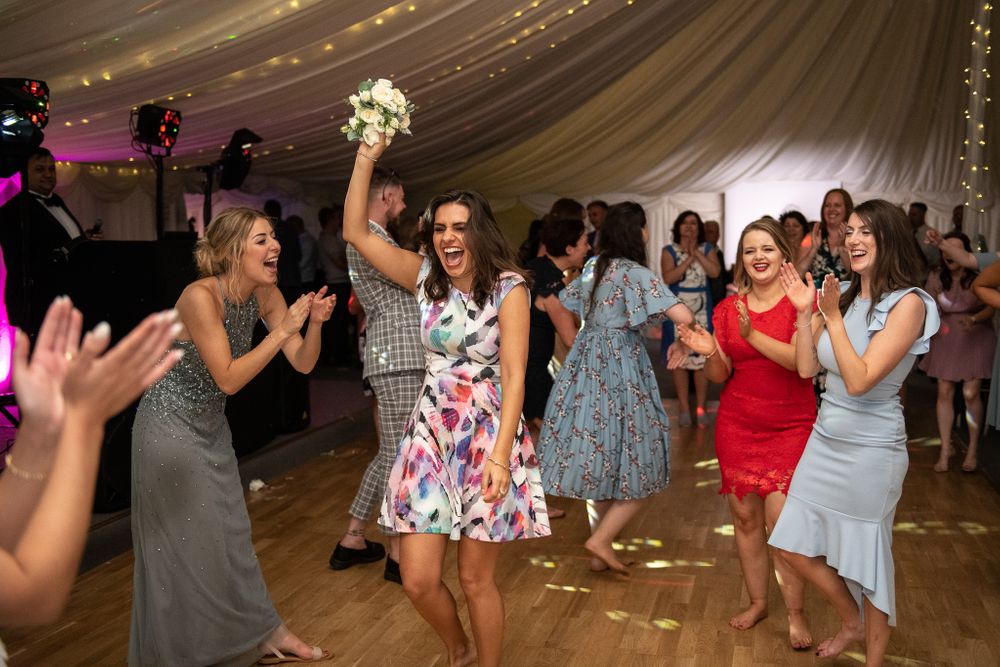 Guests enjoying a lively dance party under string lights at an indoor wedding reception venue.