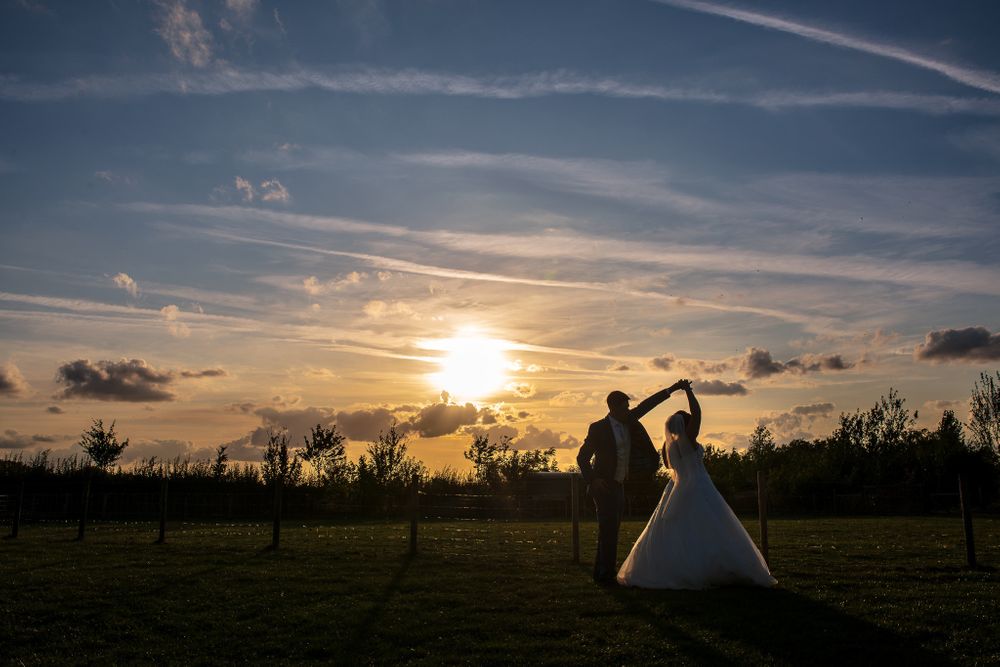 Beautiful sunset silhouettes against a dramatic sky during an outdoor wedding photo session.