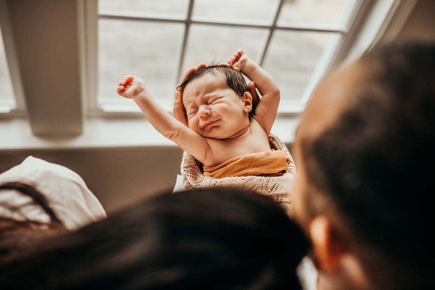 Parents look down at their baby as he stretches.
